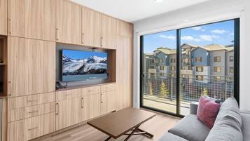 Een moderne woonkamer met een flatscreen televisie bevestigd aan een houten wand, een grijze bank met een rode kussen en een houten salontafel.