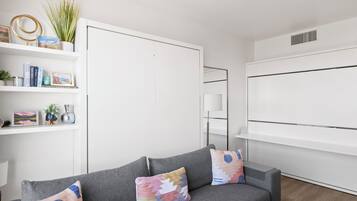 Een moderne woonkamer met een grijze bank, kleurrijke kussens, een witte boekenkast en een witte garderobe.