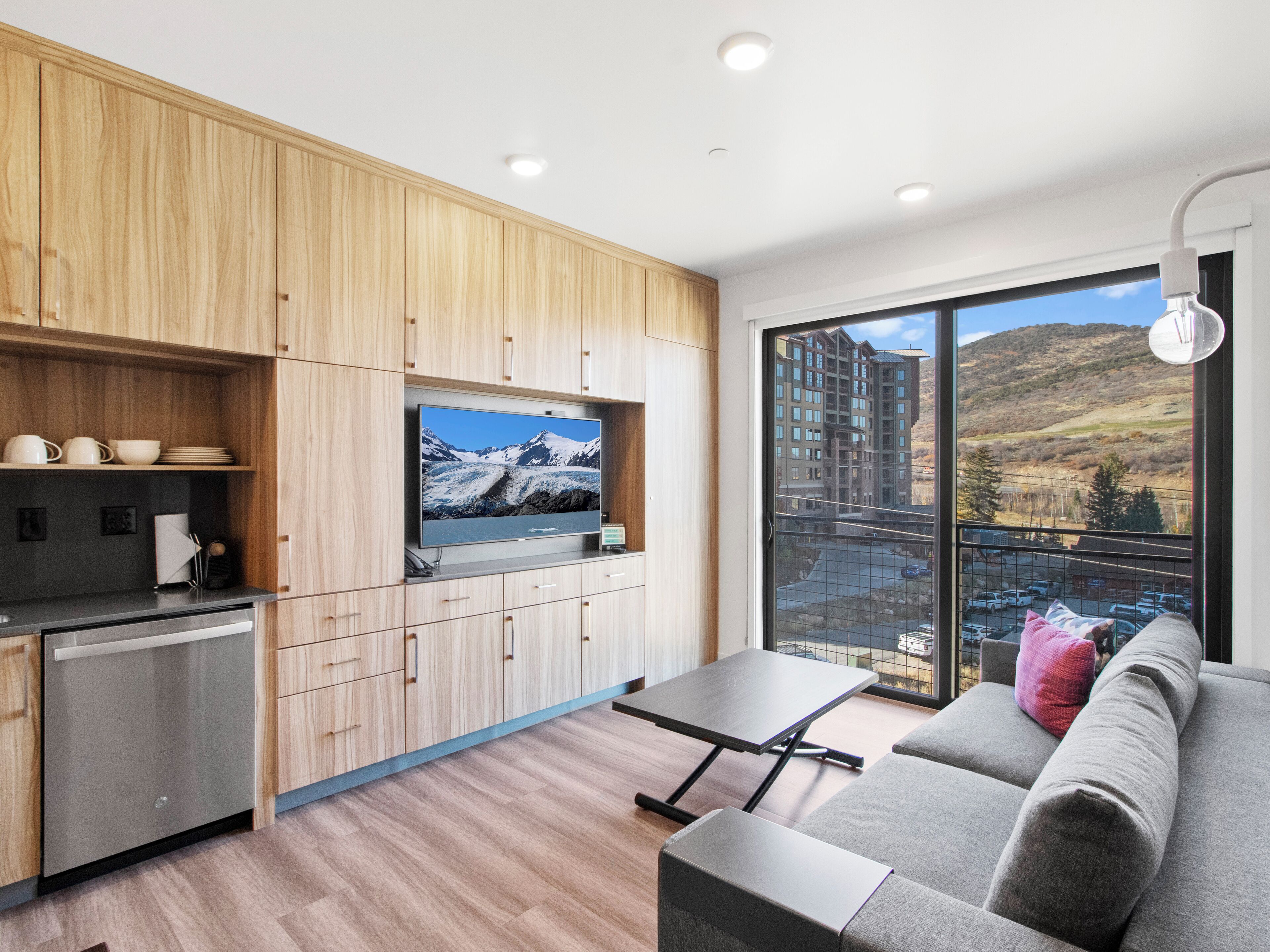 Una cocina moderna con armarios de madera, un televisor integrado y un comedor con un sofá gris y una mesa.