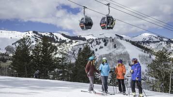 A ski lift with four chairs, a snowy mountain backdrop, and skiers on the slope.