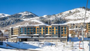 A modern hotel with multiple floors, large windows, and a ski lift in the background.
