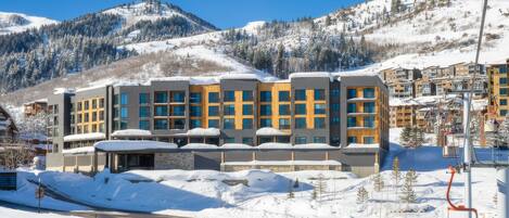 A modern hotel with multiple floors, large windows, and a ski lift in the background.