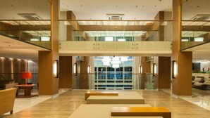 Een ruime lobby met een hoge plafond, een centrale trap en een zithoek met een rode lamp.