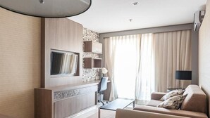 Een moderne hotelkamer met een flatscreen televisie aan een houten wand, een bank, een salontafel en een lamp.