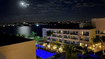 Um hotel com área de piscina, palmeiras e vista para o mar à noite.