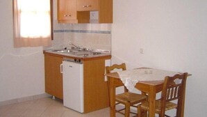A compact kitchen with a built-in dishwasher, wooden cabinets, and a dining table with chairs. - Anemoessa (Karpathos)