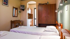A hotel room with two beds, a wooden wardrobe, a small table with a lamp, and a television on the wall. - Chrysoula (Kos)