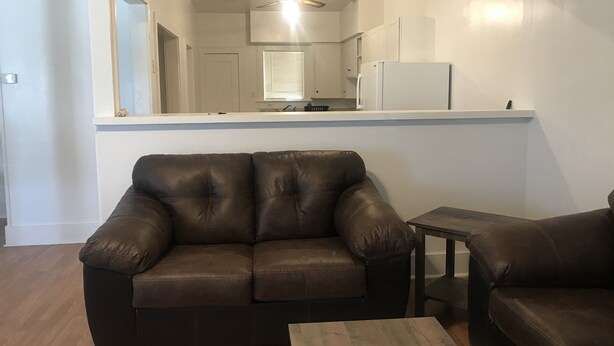 A living room with a brown leather sofa, a small wooden coffee table, and a kitchen visible through a large mirror. - Fully furnished duplex in quiet neighborhood (Sweetwater)