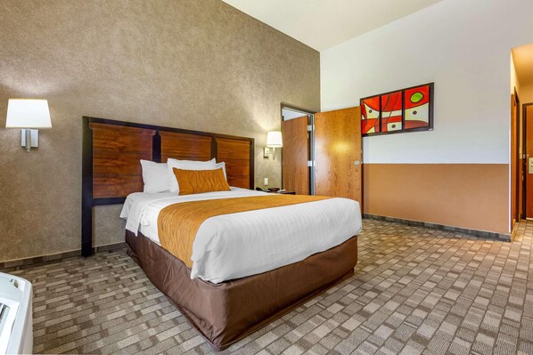 Una habitación de hotel con una cama grande, cabecera de madera, alfombra marrón, lámpara de pared y un cuadro.