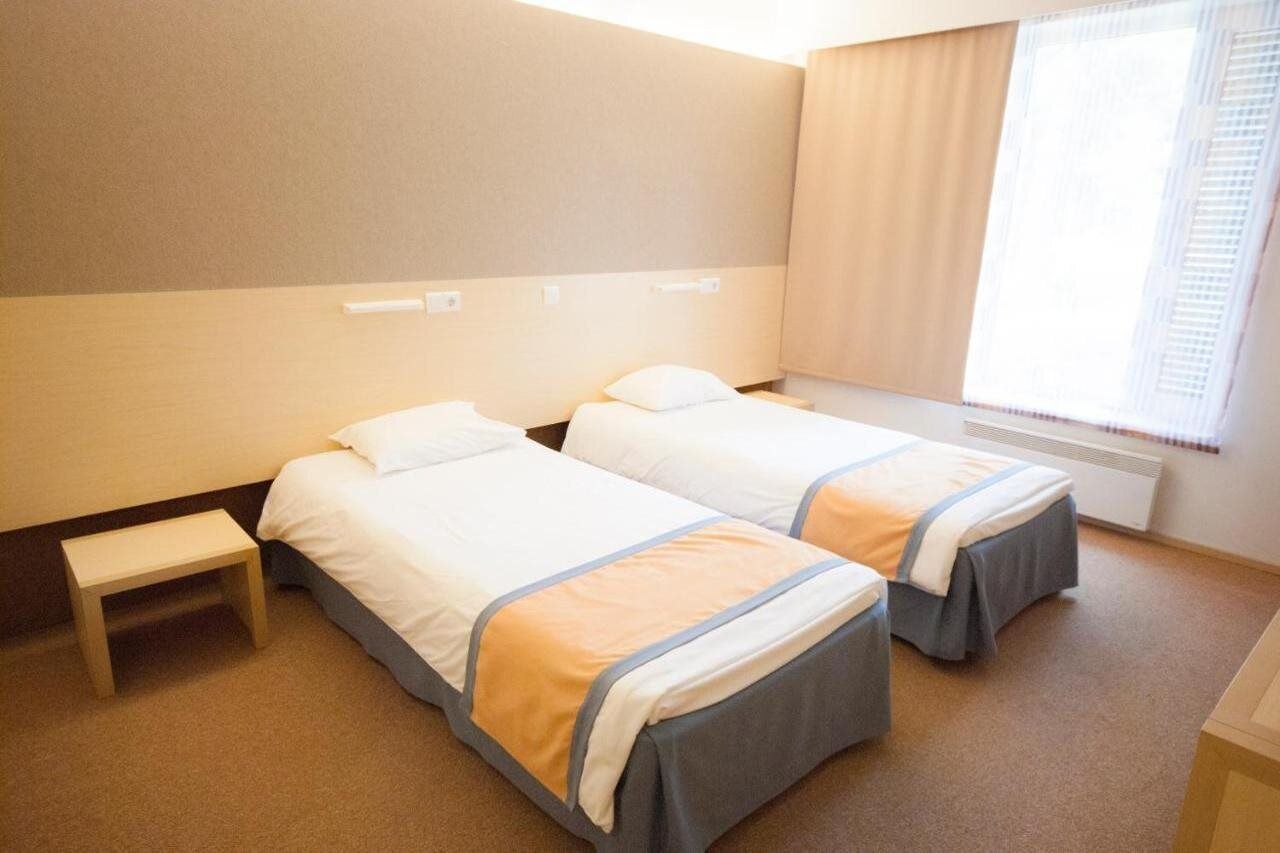 A hotel room with two beds, a small bedside table, and a window with curtains.
