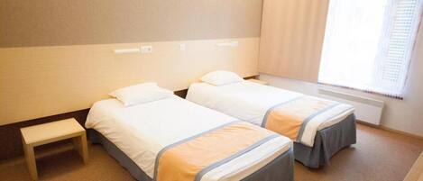 A hotel room with two beds, a small bedside table, and a window with curtains.