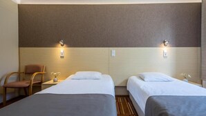 A hotel room with two single beds, a wooden chair, a small table with a vase, and wall-mounted lights. - Saarema Thalasso Spa Hotel (Mandjala)