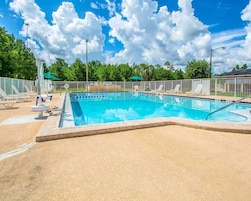 Piscina retangular com borda azulejada, rodeada por um deck de areia.