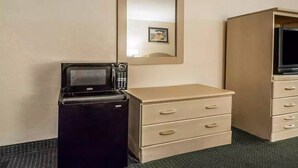 A compact room with a kitchenette area, including a refrigerator, microwave, and a small cabinet with drawers.
