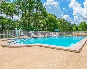 A swimming pool with a sandy deck, surrounded by a white fence, and trees in the background. - Rodeway Inn Gainesville University Area (Gainesville)
