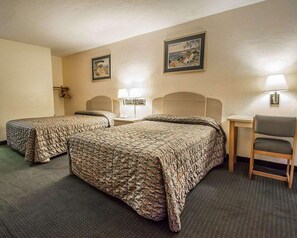 Habitación de hotel con dos camas, un escritorio, una silla y dos lámparas de pared.