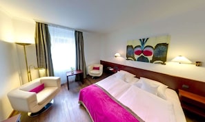 A hotel room with a bed, a chair, a desk, a lamp, and a painting on the wall. - Central (Freiburg im Breisgau)