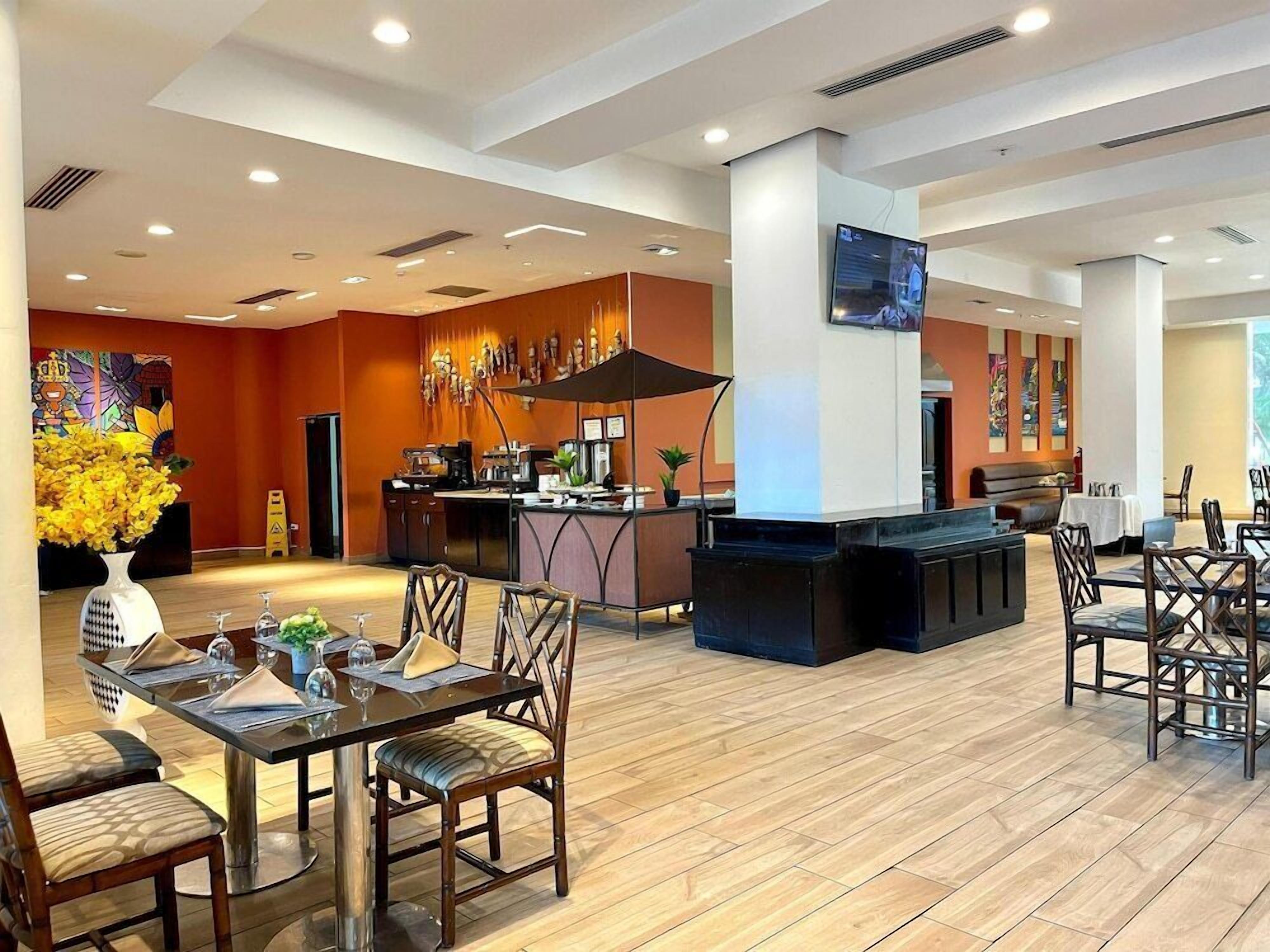 A modern hotel lobby with a central bar area, dining tables, and chairs.