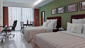 Ein Hotelzimmer mit zwei Betten, einem Schreibtisch mit Stuhl, einem Fenster mit Vorhängen und gerahmten Bildern an der Wand.