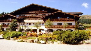 Un bâtiment de style alpin traditionnel, doté de nombreux balcons, d’un patio aménagé avec des sièges et surplombant un paysage montagneux.