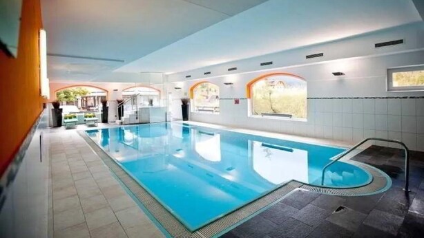 Une grande piscine intérieure à l’eau d’un bleu limpide, entourée de murs et d’un sol recouverts de carreaux.