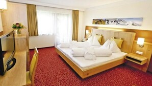 Une chambre d’hôtel avec un grand lit, une télévision, un bureau et une fenêtre avec des rideaux.