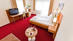 Une chambre d’hôtel avec un lit, un bureau avec un ordinateur portable, une petite table avec une assiette et des verres, et une télévision.