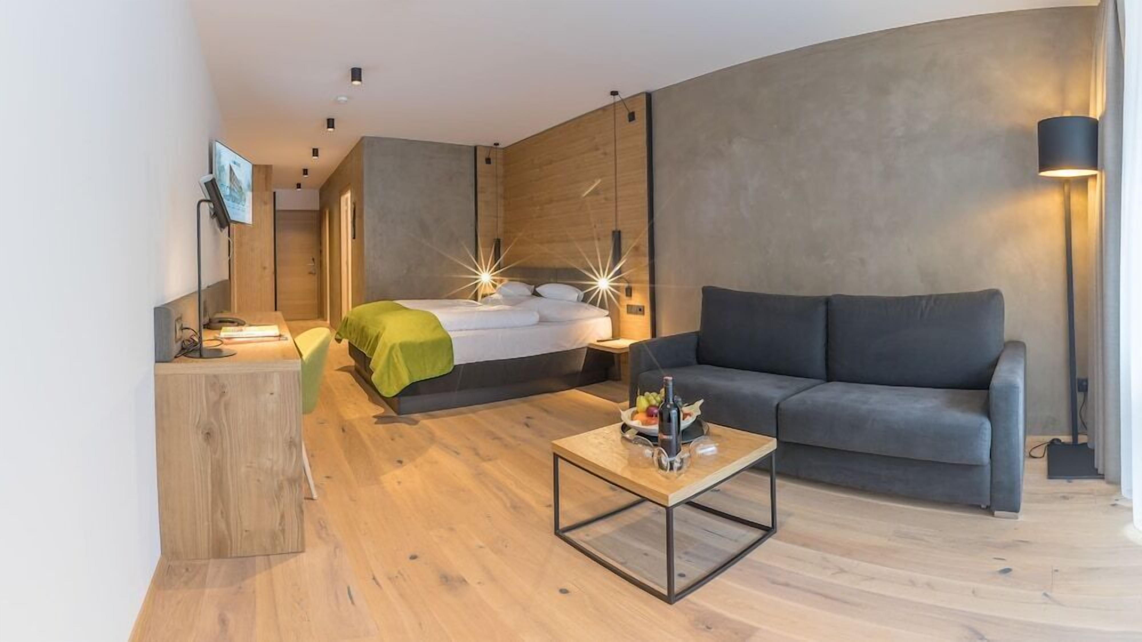 Una habitación de hotel moderna con cama, sofá, mesita de centro y escritorio.