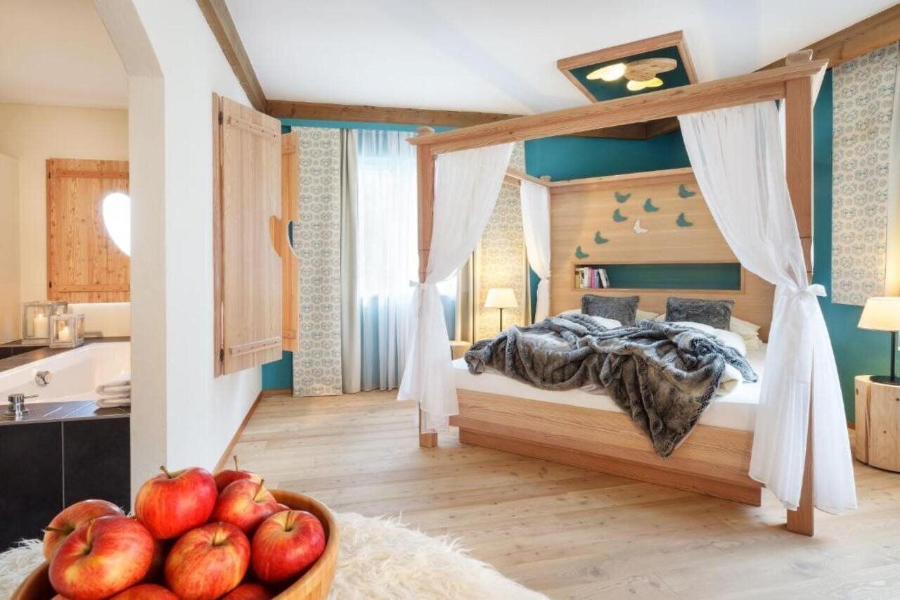 Ein Schlafzimmer mit einem hölzernen Himmelbett, einem Nachttisch, einer Wandregal mit Büchern und einem Beistelltisch.