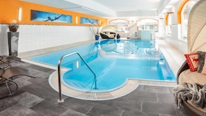 Una piscina interior con vista a agua cristalina, un área de descanso con una silla y una toalla, y una pared con una obra de arte azul.