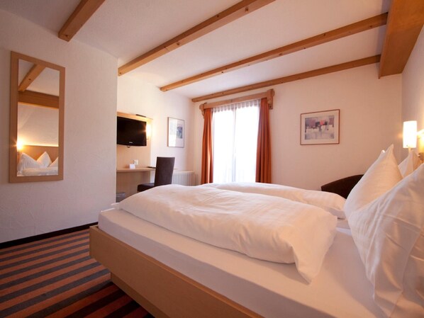 Habitació d'hotel amb un llit gran, una escriptori amb una cadira, una televisió i una finestra amb cortines.