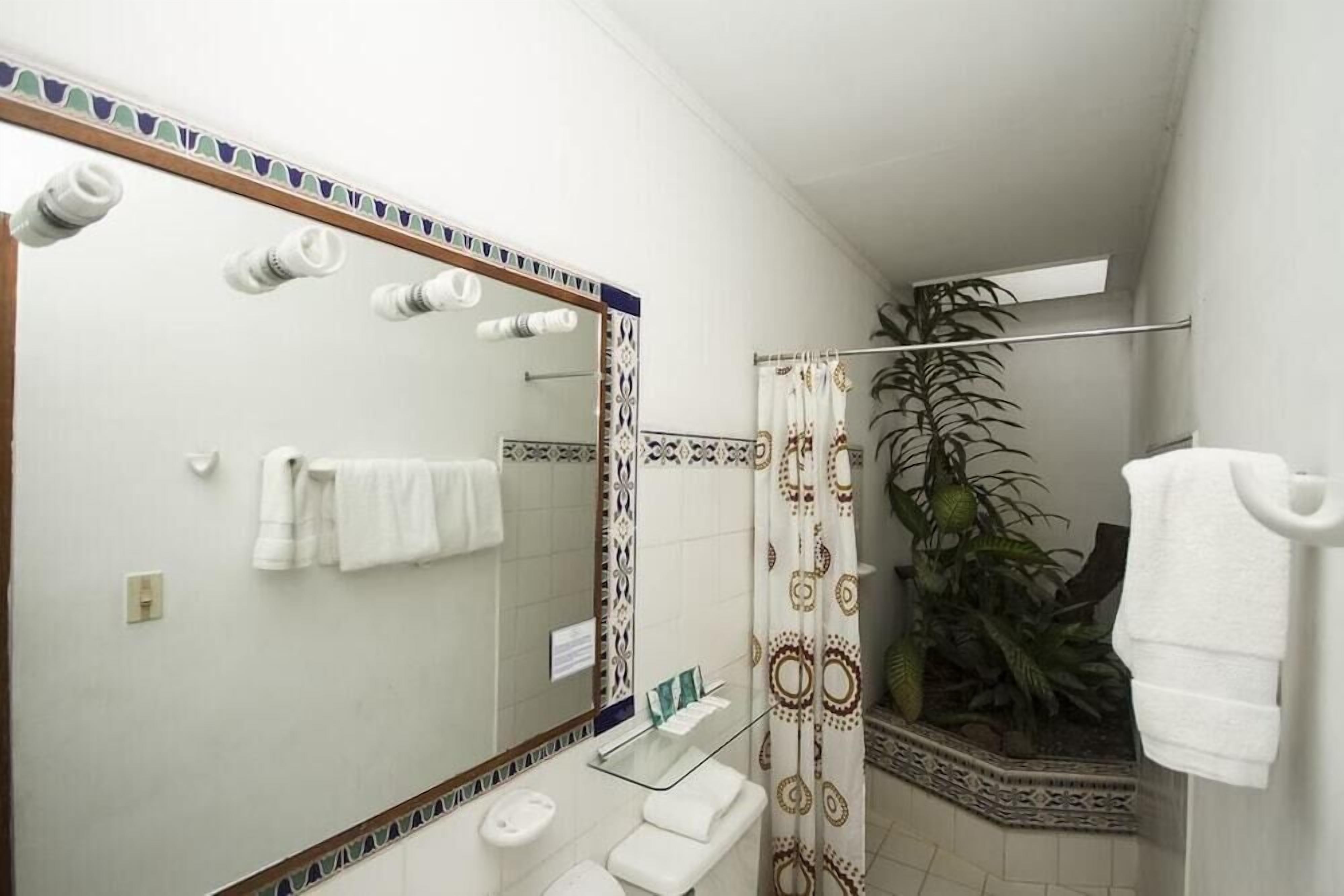A bathroom with a large mirror, white towels, a glass shower enclosure, and a potted plant.