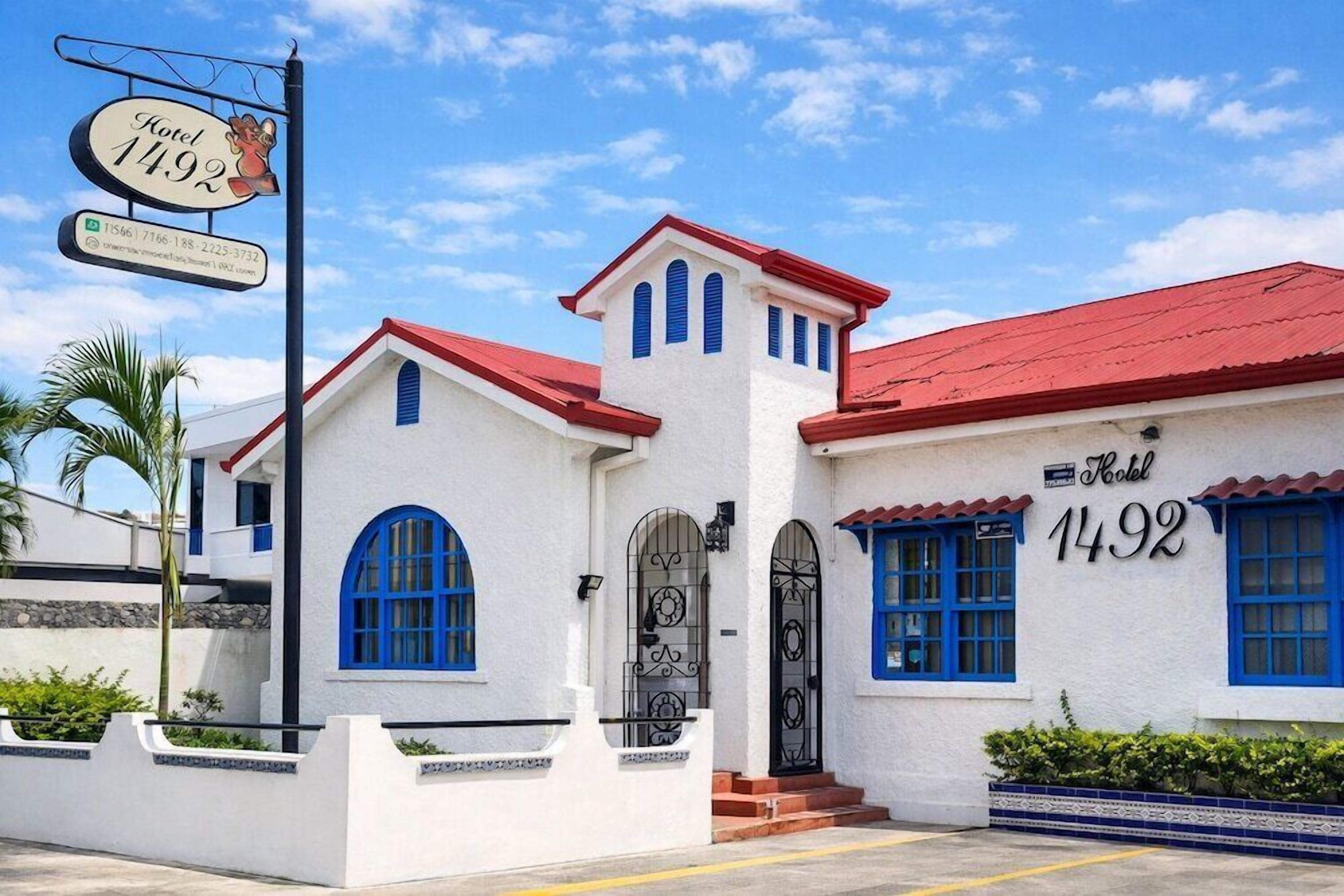 A white building with blue accents and a red roof, marked as Hotel 1492.