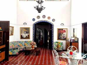 A room with a patterned floor, a sofa, a dining table with chairs, and a chandelier. - 1492 Hotel (San José)