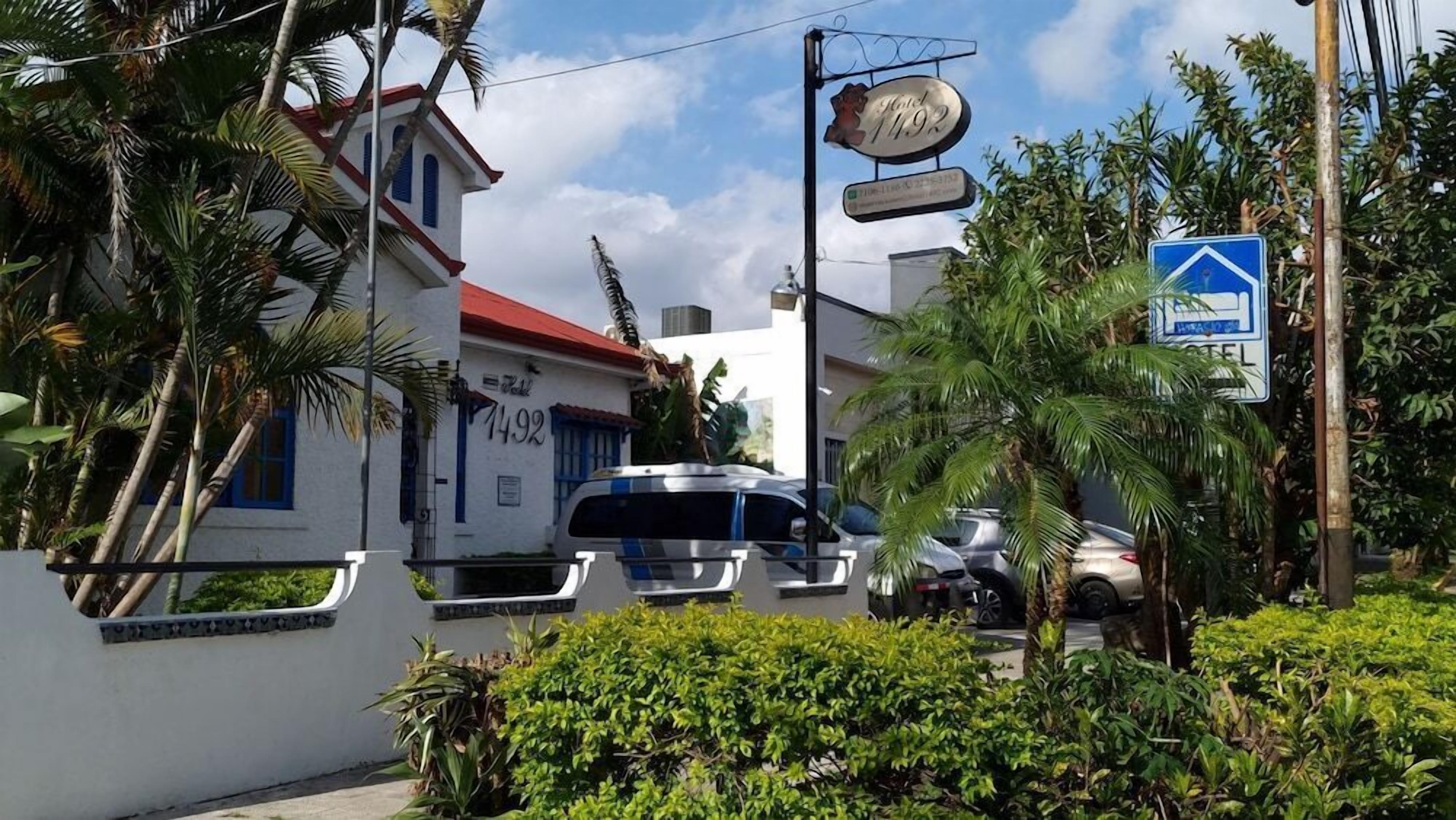 A building with a red roof and blue windows, a sign for a hotel, and a blue directional sign.