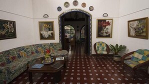 Un salón con un sofá estampado, una mesa de centro y dos sillones. Hay obras enmarcadas en las paredes y un arco decorativo.