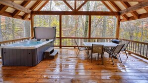 Eine Holzterrasse mit Whirlpool, Tisch und Stühlen mit Blick auf einen Wald.
