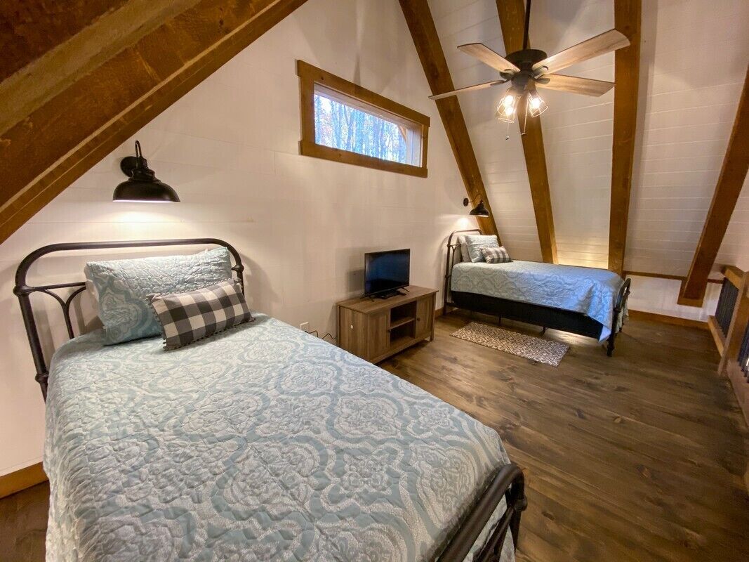 A cozy attic bedroom with two beds, a ceiling fan, and a small TV.