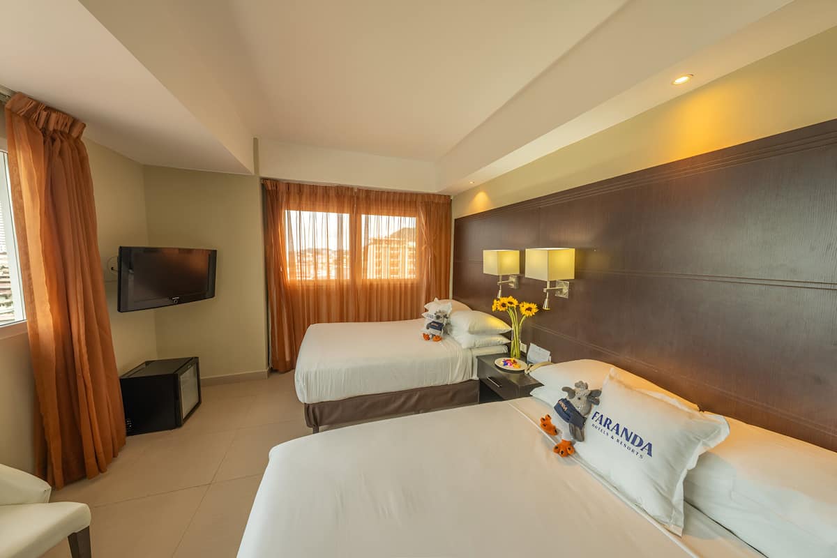 A hotel room with two beds, a TV, a desk, and a window with curtains.