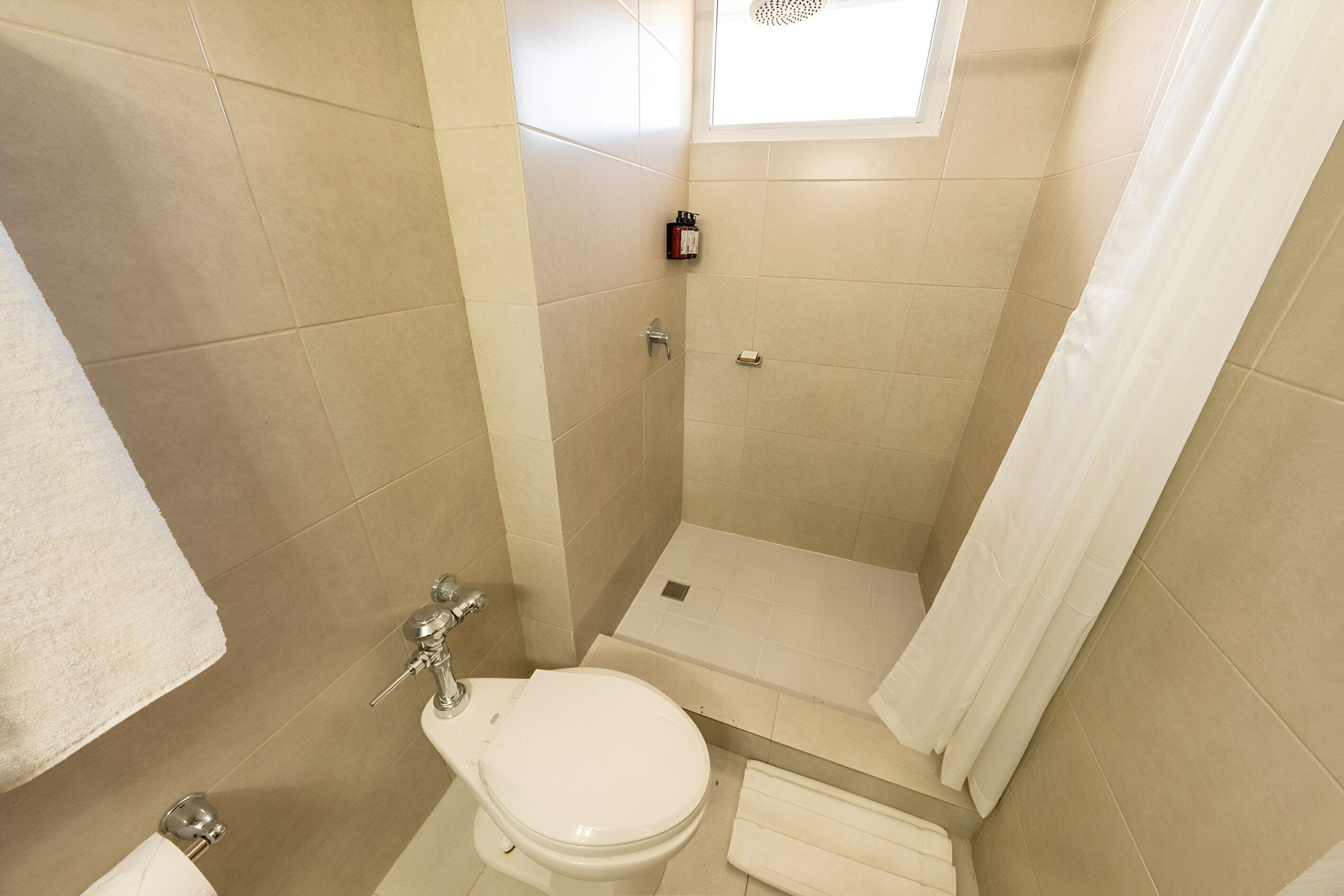 Een kleine badkamer met tegels, voorzien van toilet, douche en een raam.
