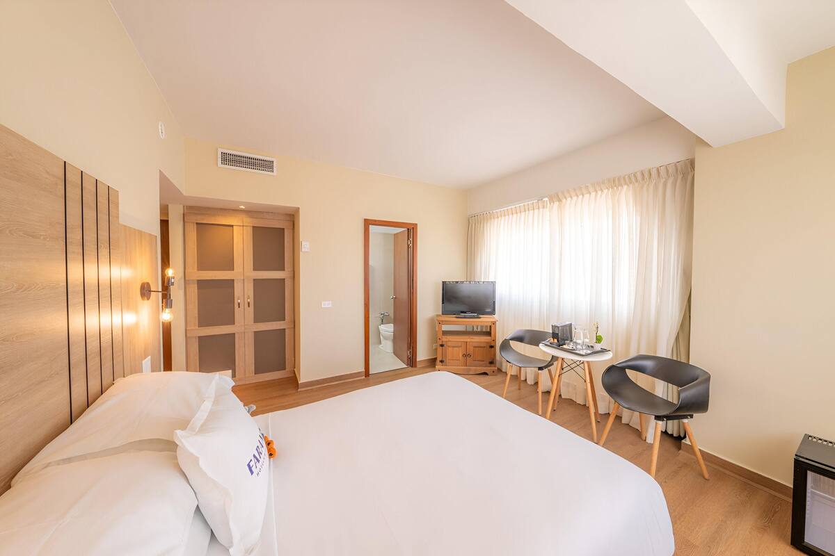 A hotel room with a large bed, a desk with a chair, a television, and a bathroom visible through an open door.