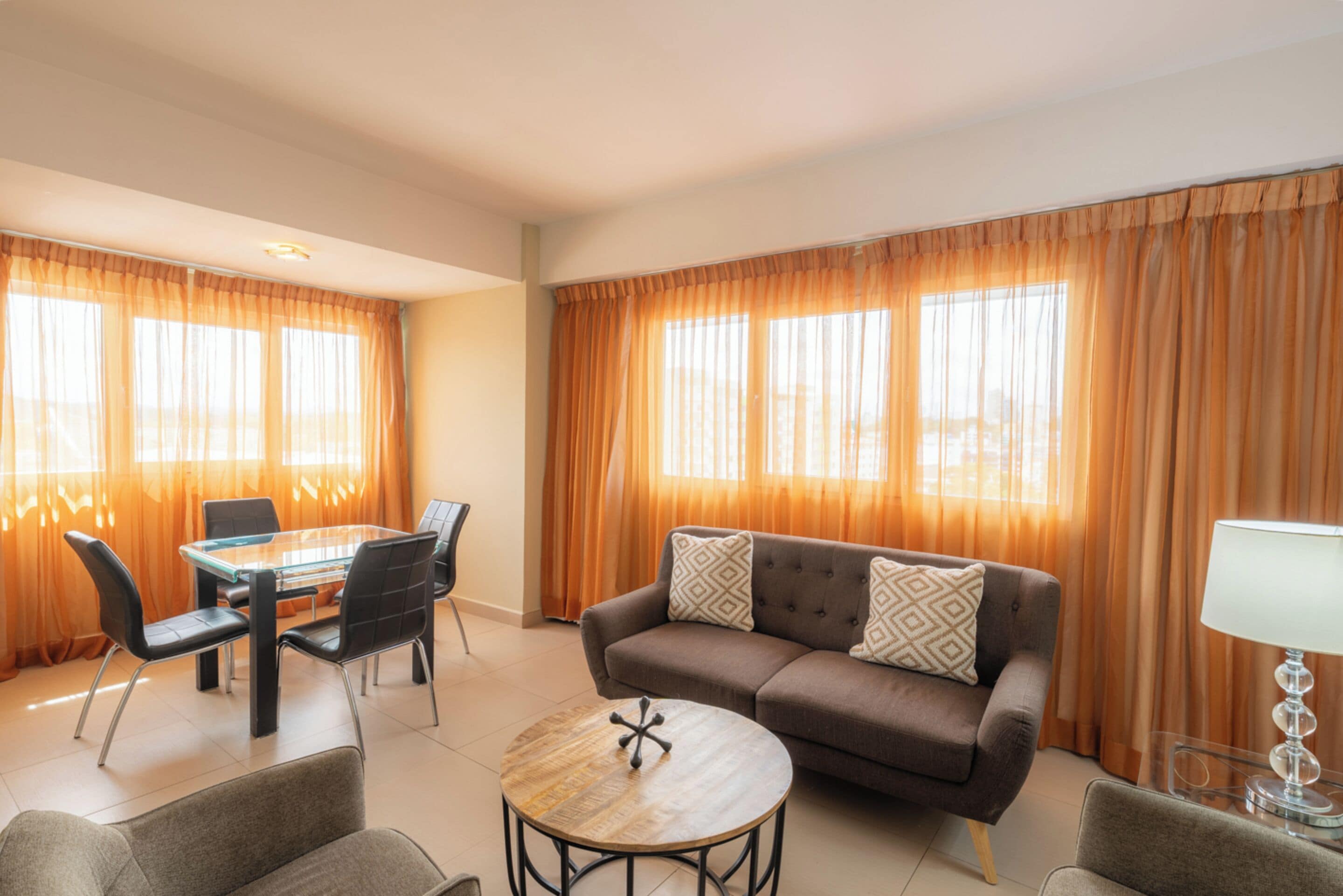 A modern living room with a glass-top dining table, a brown sofa with patterned cushions, and a round coffee table.