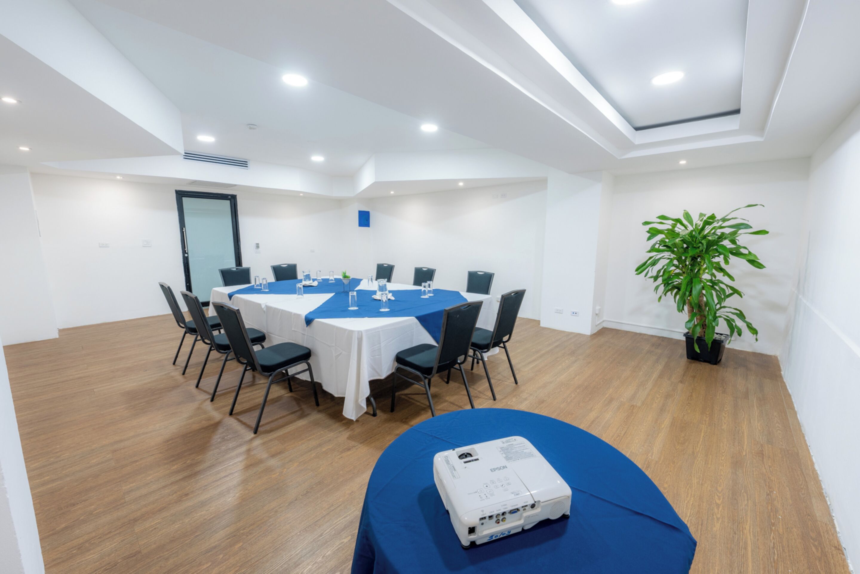 A conference room with a round table, chairs, a projector, and a potted plant.