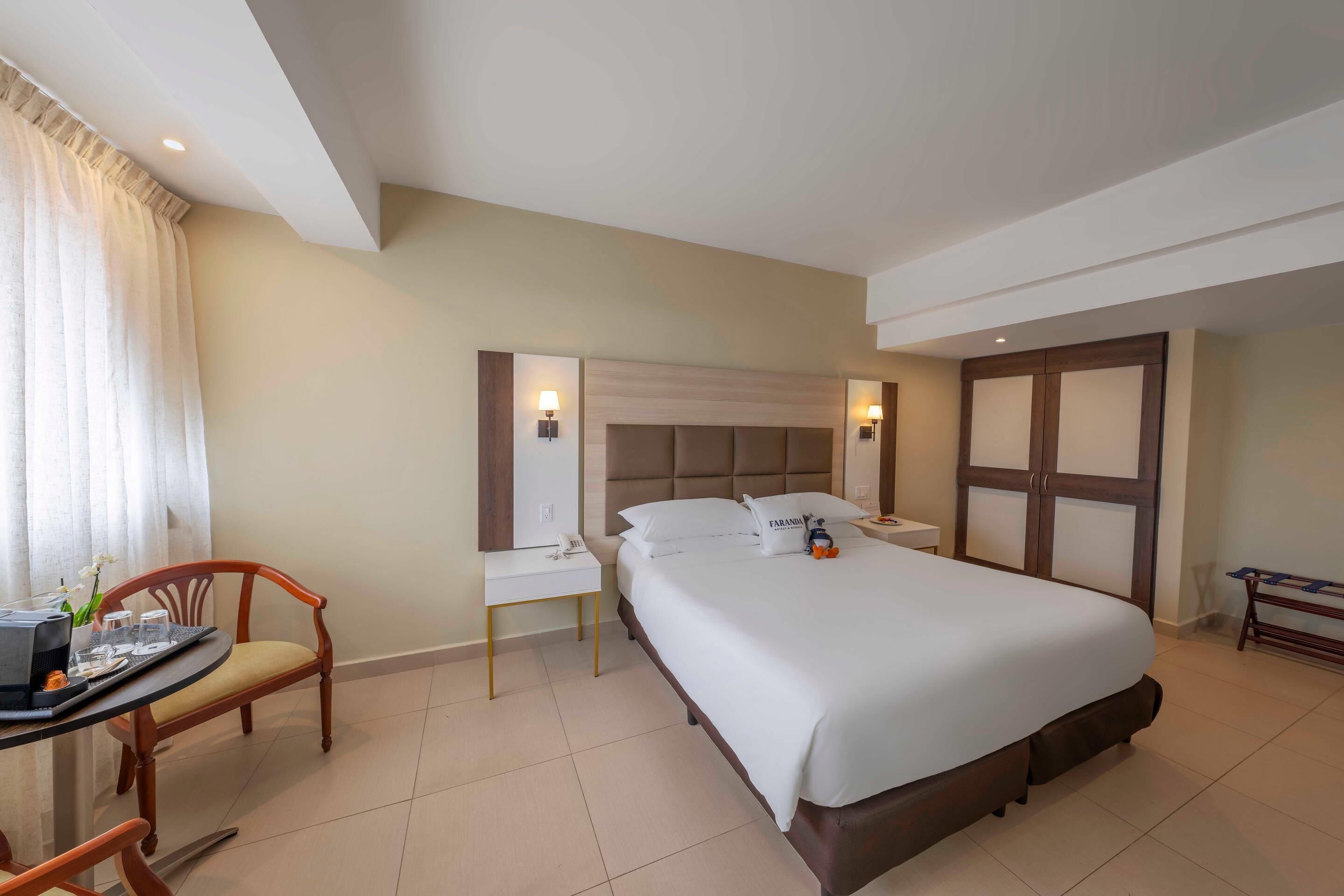 Habitación de hotel con una cama grande, un escritorio con silla, una mesita de noche y un armario.