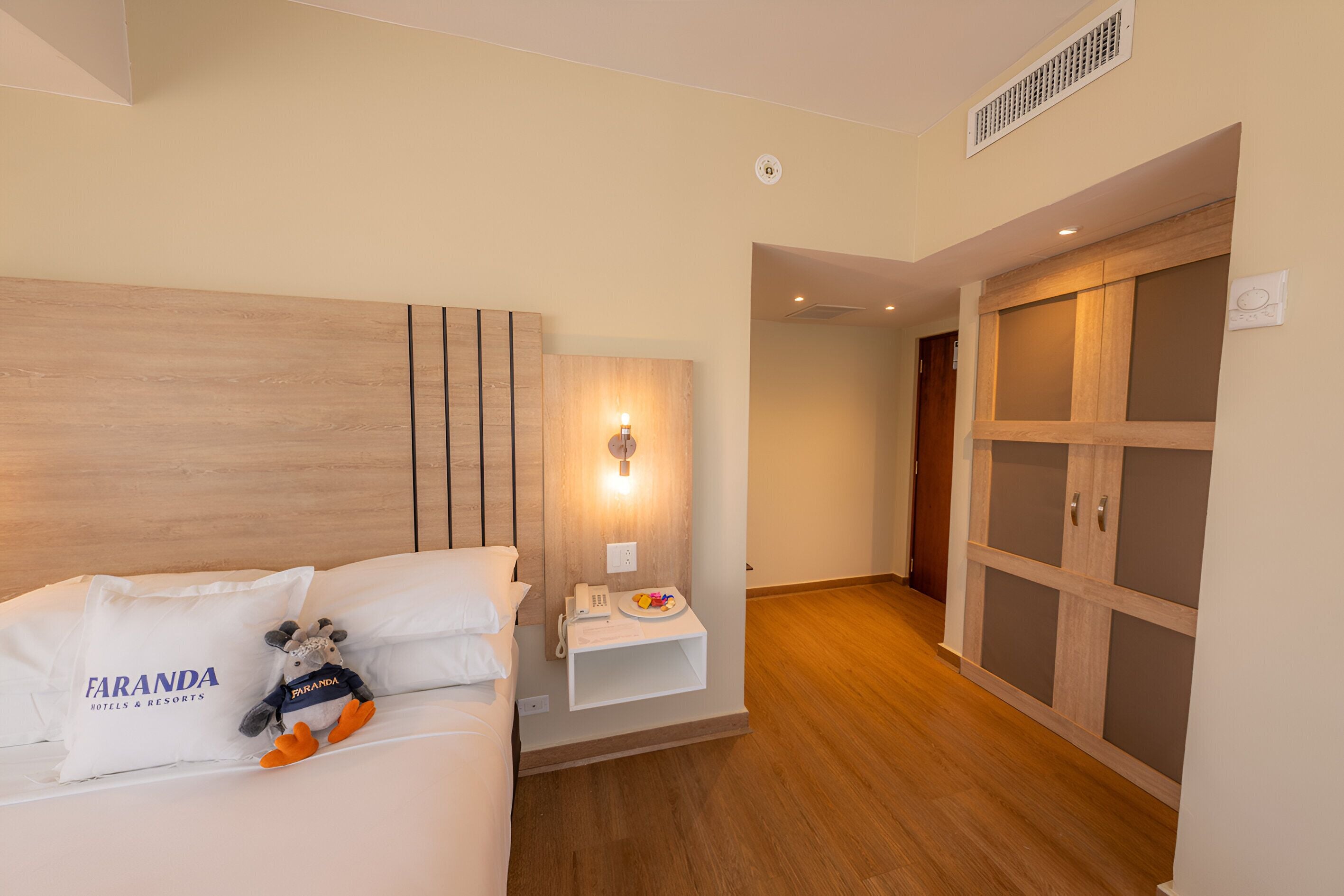 Une chambre d’hôtel comprenant un lit, une table de chevet, une lampe fixée au mur et une armoire.