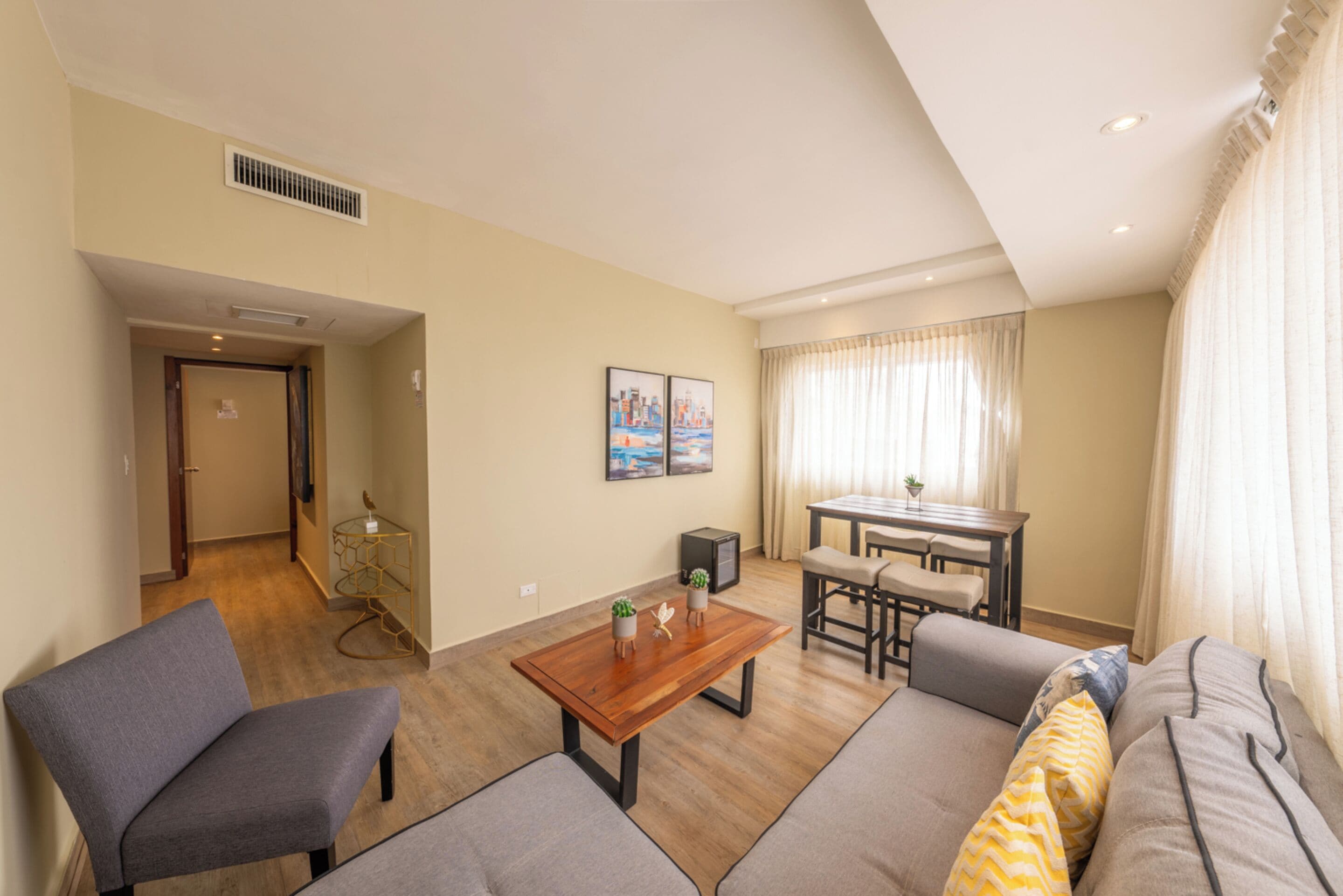 A modern living room with a sofa, armchair, and a wooden coffee table. There is a dining area with a table and chairs.