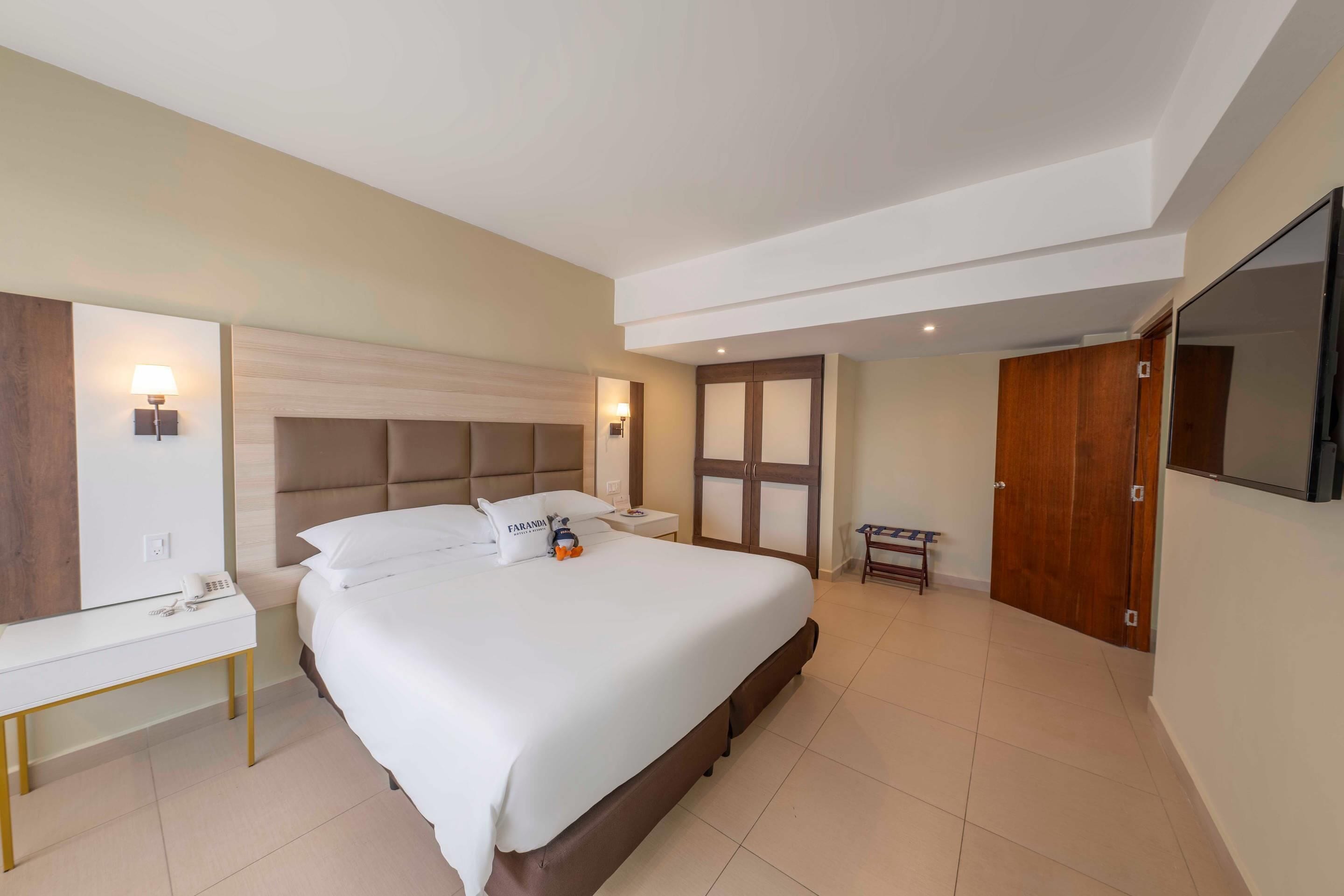 Habitación de hotel con una cama grande, mesitas de noche, un armario, un espejo y un televisor de pantalla plana.