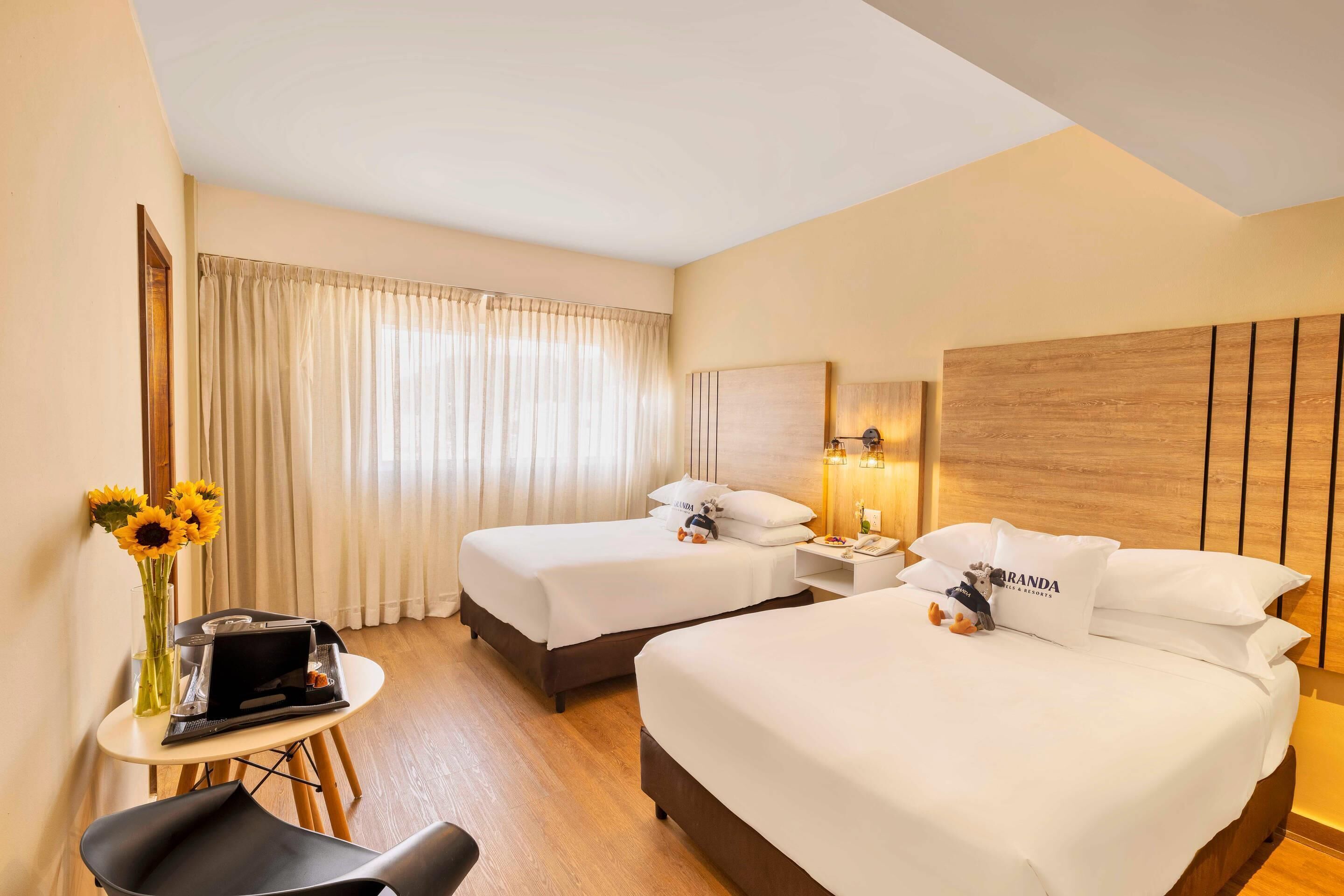 Habitación de hotel con dos camas, un escritorio, una silla y un florero con girasoles.