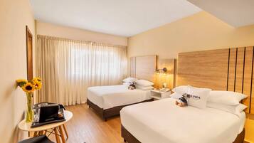 Habitación de hotel con dos camas, un escritorio, una silla y un florero con girasoles.