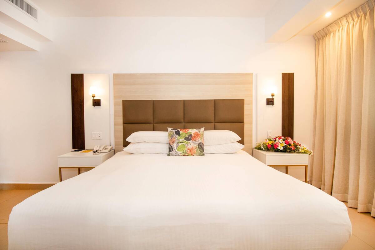 A large bed with a wooden headboard, two bedside tables, and a floral arrangement on one of the tables.